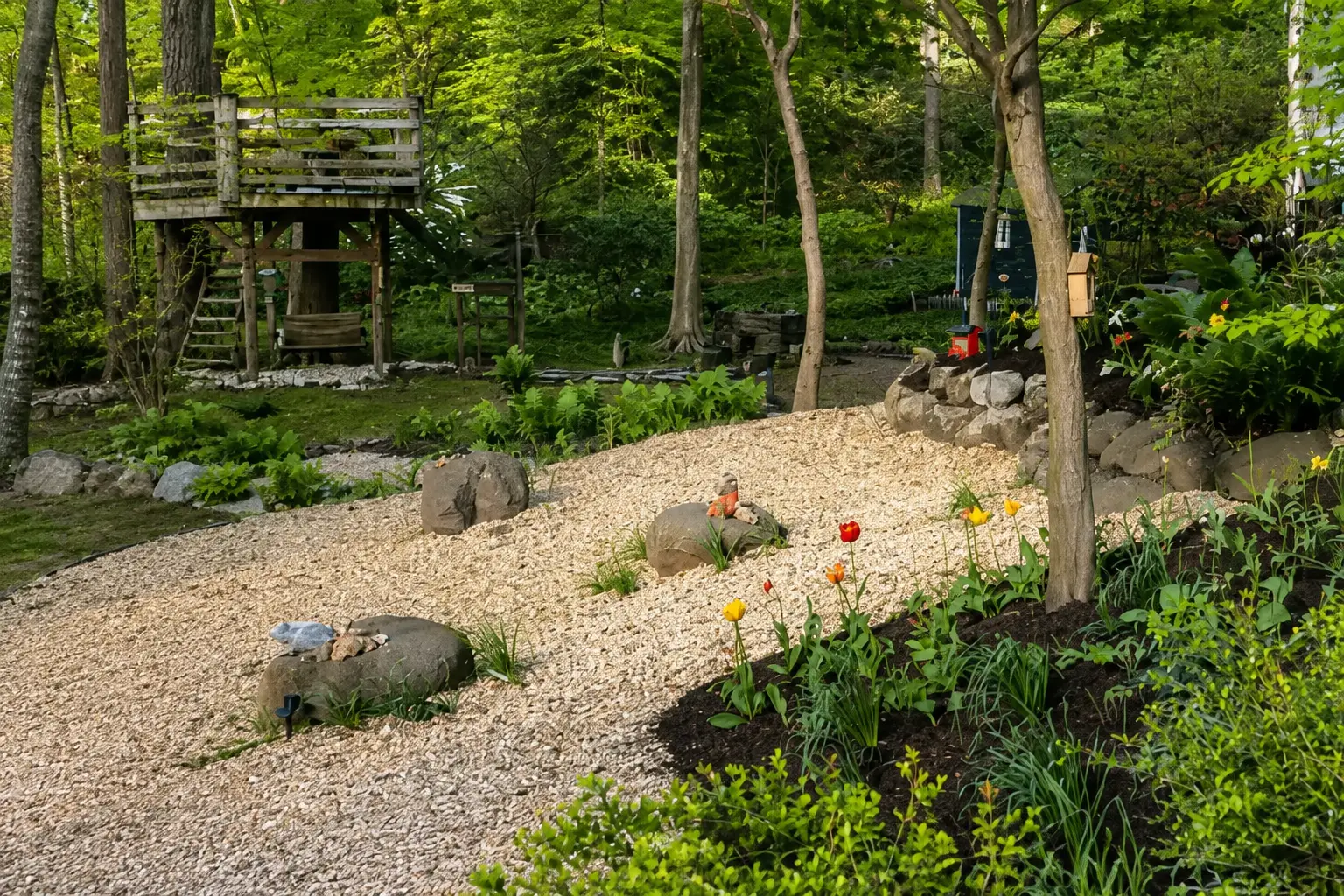 A woodland garden with a gravel path, established trees, rocks and planting